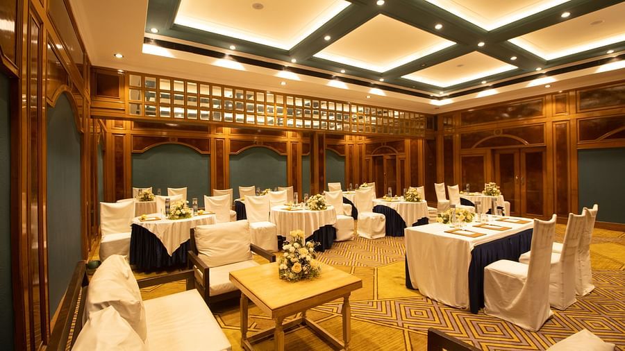 Luxurious banquet space with intricate carpet design, wood-paneled walls, round tables with formal settings, and ambient ceiling lighting.
