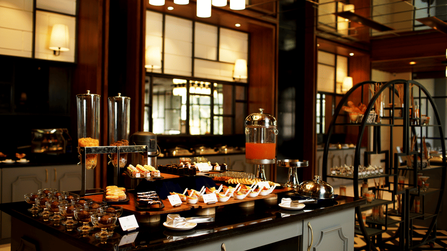 Buffet counter at Polo Hotel, Agartala with juice dispensers, desserts in glasses, plated bites, pendant lights and a black metal display rack.