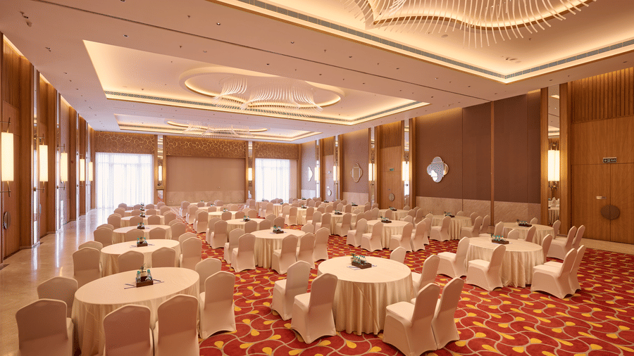 Grand hall at Prachi Sarovar Premiere, Bhubaneswar, arranged with several round tables and chairs on patterned carpeting under modern lighting.