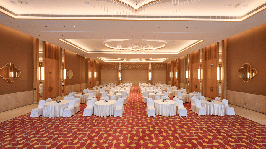 Spacious ballroom at Prachi Sarovar Premiere, Bhubaneswar, set up with round dining tables and chairs on a geometric-patterned carpet.