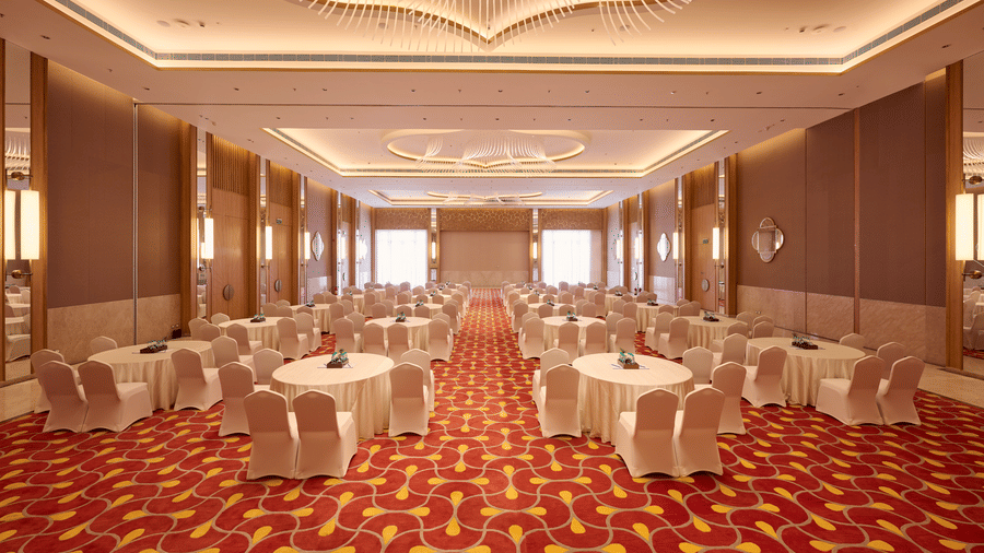 Event venue at Prachi Sarovar Premiere, Bhubaneswar, arranged with multiple round tables and chairs, patterned flooring, and wall panels.