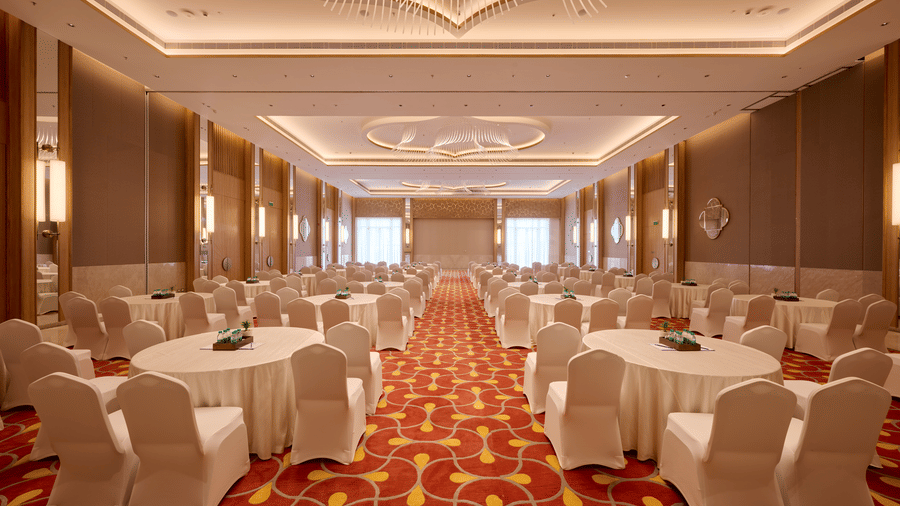 Banquet setup at Prachi Sarovar Premiere, Bhubaneswar, featuring multiple round tables with chairs, a patterned carpet, and wall panels.