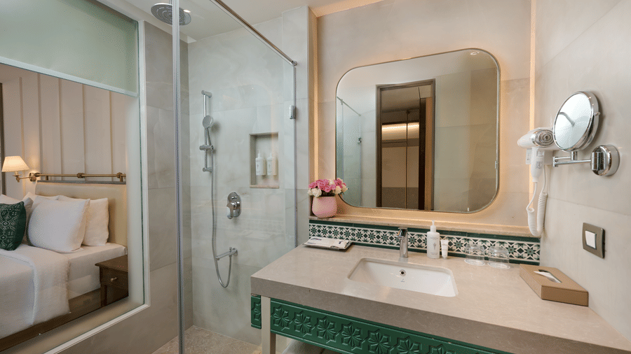 Deluxe King Room's bathroom at Prachi Sarovar Premiere, Bhubaneswar, featuring a vanity sink, a wall mirror, and a glass-enclosed shower stall.