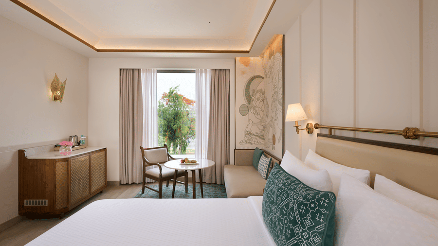Deluxe King Room at Prachi Sarovar Premiere, Bhubaneswar, displaying a bed with pillows, a wooden cabinet, a chair, and a large window.
