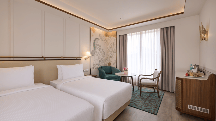 Deluxe Twin Room at Prachi Sarovar Premiere, Bhubaneswar, featuring 2 single beds, a wooden cabinet, an armchair, and a window with curtains.