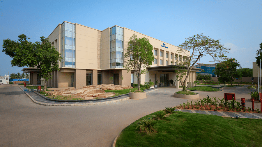 Daytime exterior view of Prachi Sarovar Premiere, Bhubaneswar, with an asphalt driveway, green lawns, young trees, and the main hotel building.
