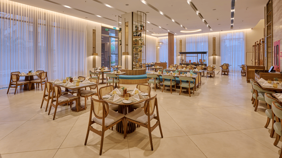 Spacious Flavours dining room at Prachi Sarovar Premiere, Bhubaneswar, arranged with multiple wooden dining tables and chairs under a brightly lit ceiling.