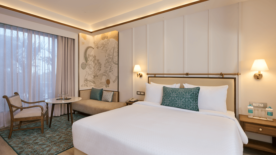 Premium Room at Prachi Sarovar Premiere, Bhubaneswar, with a large bed, wall lamps, a sofa, an armchair, and glass doors leading outside.