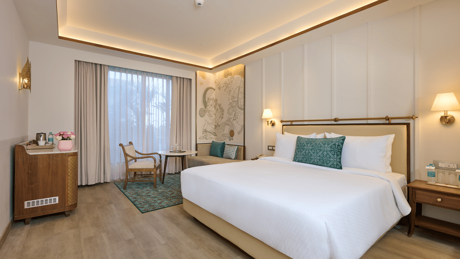 A Premium Room's bedroom at Prachi Sarovar Premiere, Bhubaneswar, featuring a bed, bedside tables with lamps, a wooden cabinet, and a curtained window.