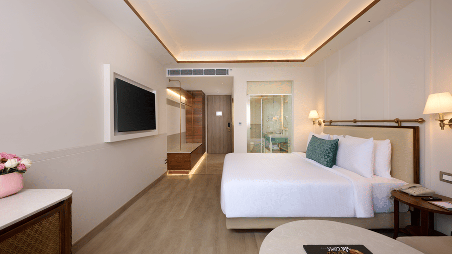 Standard Room at Prachi Sarovar Premiere, Bhubaneswar, with a bed, a wall-mounted television, a round table, and an entrance corridor.