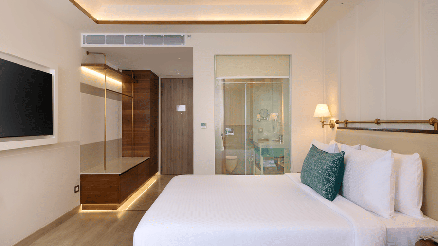 Standard Room at Prachi Sarovar Premiere, Bhubaneswar, with a bed, a wall television, a wardrobe area, and a glass bathroom partition.