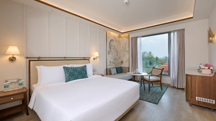Standard Room view at Prachi Sarovar Premiere, Bhubaneswar, featuring a bed with pillows, bedside tables, a seating area, and a large window.