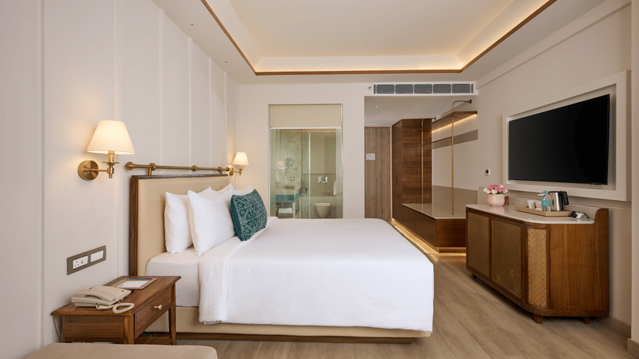 Superior Double Room at Prachi Sarovar Premiere, Bhubaneswar, with a large bed, wall lamps, a television, a wooden cabinet, and wardrobe doors.