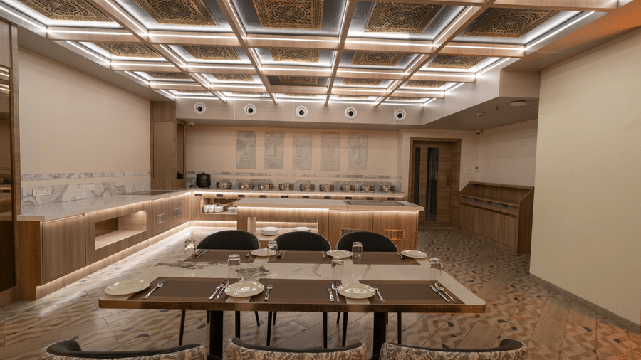 A brightly lit dining room with a buffet area, a seating area and a patterned ceiling with integrated linear lighting | Pride Elite Chhatrapati Sambhajinagar
