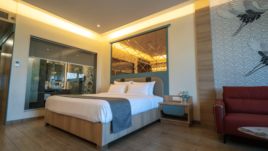 A hotel room featuring a double bed, a red armchair, and a decorative wall panel with a reflective surface | Pride Elite Chhatrapati Sambhajinagar