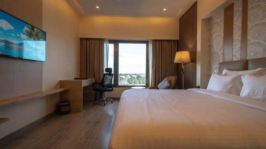A hotel room featuring a double bed with white bedding, a wall-mounted TV, and a large window in the background | Pride Elite Chhatrapati Sambhajinagar