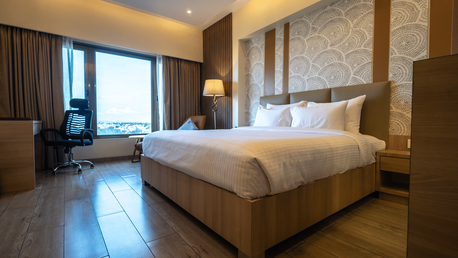 A modern hotel room featuring a double bed, a lit bed side lamp, and a large window with city views | Pride Elite Chhatrapati Sambhajinagar
