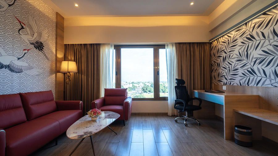 Living area of the Suite with a red sofa, a small armchair, a desk, and a large window with outdoor views | Pride Elite Chhatrapati Sambhajinagar
