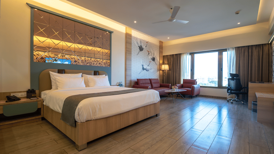 A spacious hotel room featuring a double bed, a small seating area with a red sofa, and a large window with outdoor views | Pride Elite Chhatrapati Sambhajinagar