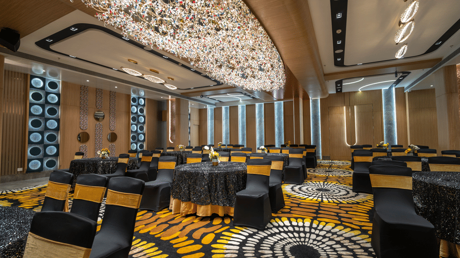 A banquet hall featuring neatly arranged cluster style seating arrangement, carpeted floors and a grand linear chandelier | Pride Elite Chhatrapati Sambhajinagar