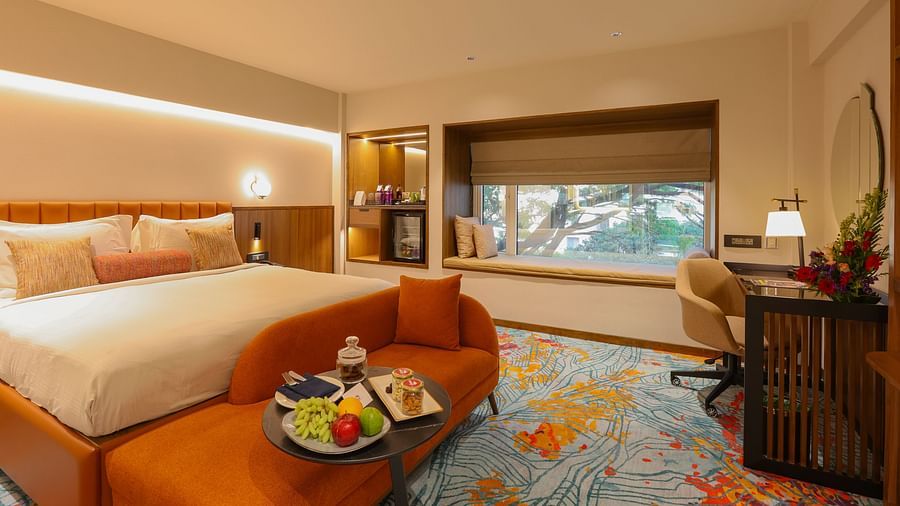 A hotel room with a bed, a couch, and a view of the outside - Pride Hotel Pune