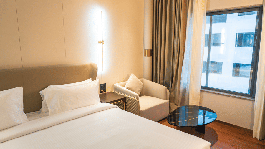 A comfortable king size bed, a lounge chair, and a window with drapes at Pride Plaza Indore.