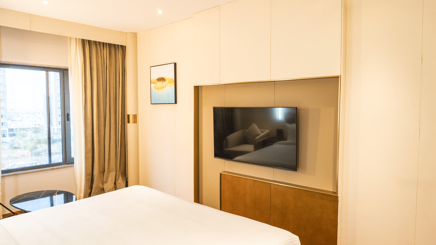 A wall-mounted television, a large king size bed, and a window with curtains at Pride Plaza Indore.