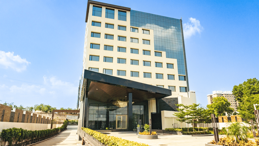 A ground-level exterior view showing a multi-storey hotel building, a wide entrance canopy, and a stone paved courtyard at Pride Plaza Indore.