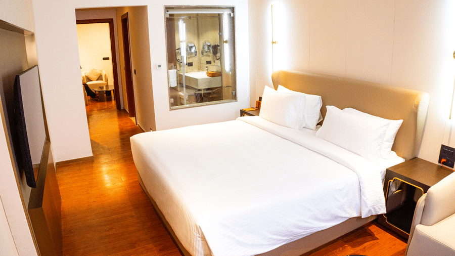 A king size bed, a wall-mounted television, and a glass-walled bathroom at Pride Plaza Indore.