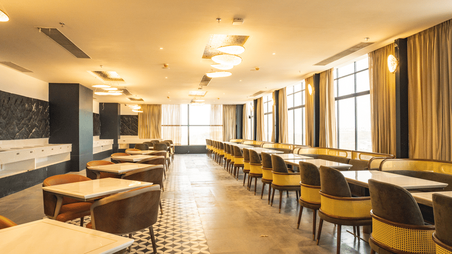 A wide dining area displaying structured tables, chairs, and large windows at Pride Plaza Indore.