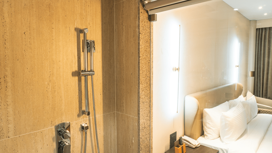 A modern shower fixture, marble walls, and a view into the bedroom at Pride Plaza Indore.