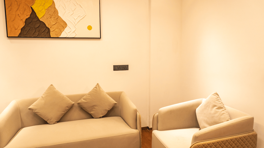 A fabric sofa, a matching armchair, and a modern painting on the wall at Pride Plaza Indore.