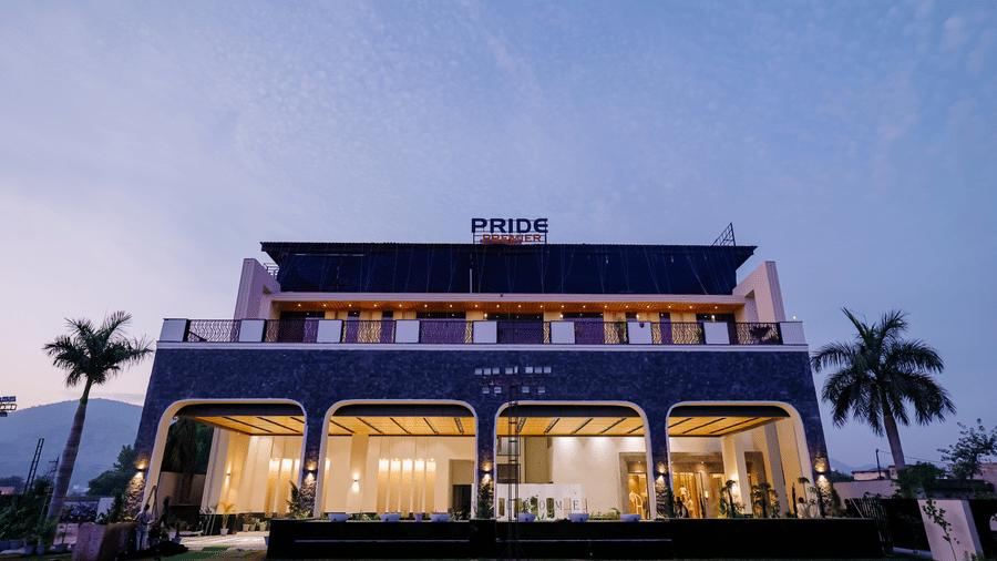Pride Premier Alwar| The illuminated facade of the property with the building and trees around it.