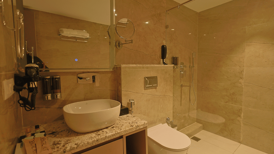 Pride Premier Alwar | A bathrrom with a bathtub, a sink, a toilet seat, and other toileteries.