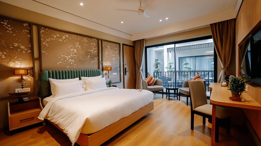 Pride Premier Alwar | A room with a large bed, bedspreads, pillows, a table, and windows with curtains.