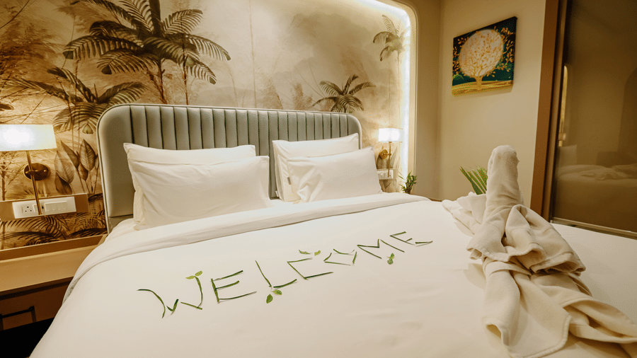 Pride Premier Alwar | A room with a bed, bedspreads, pillows, with written welcome, lamp, and a wall art.