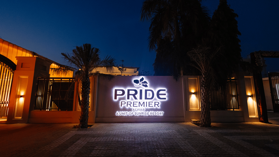 Pride Premier Alwar- Illuminated hotel exterior at dusk featuring a large sign for a premier hospitality brand.