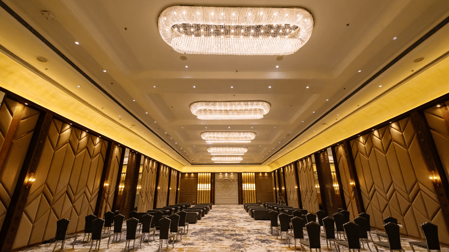 Pride Premier Alwar | a banquet hall with several chairs, decorated walls and chandeliers.