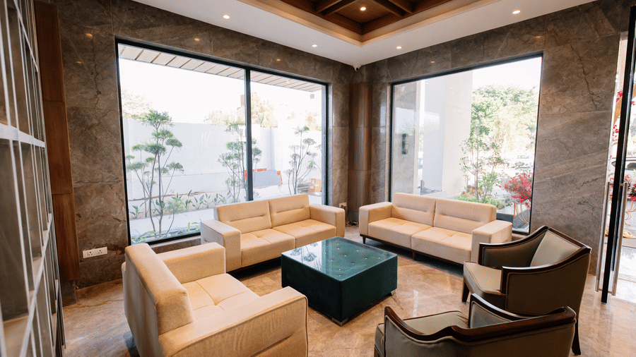 Pride Premier Alwar | Lobby with several cushions, table, and windows.
