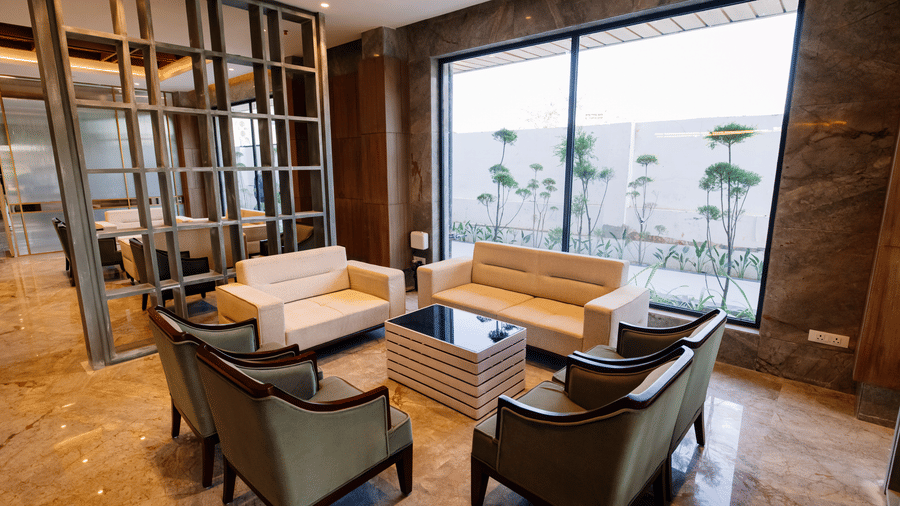 Pride Premier Alwar | Lobby with several cushions, table, and windows.