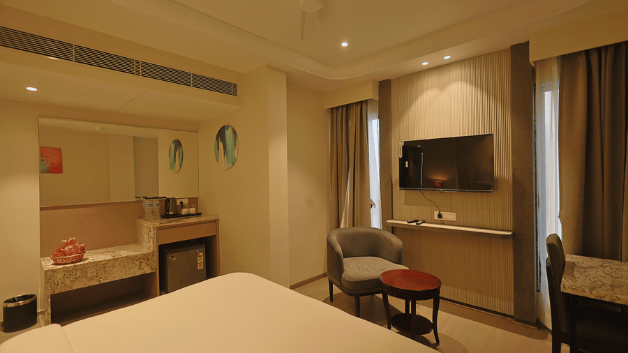 Pride Premier Alwar | A room with a large bed, spreads, chairs, and a television.