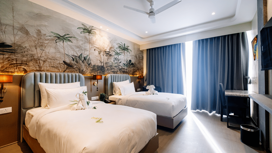 Pride Premier Alwar | A room with twin beds, bedspreads, pillows, windows covered with curtains.