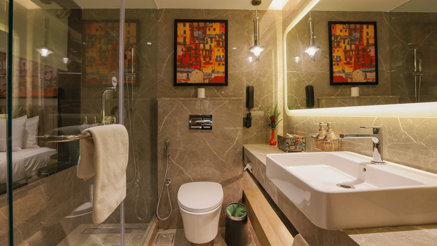 Bathroom at Pride Premier Pune with a vanity, toilet, glass shower enclosure and framed wall artwork.