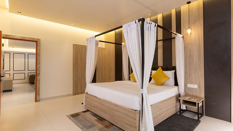 A full view of a stylish hotel bedroom dominated by a large four-poster bed with white drapes and yellow pillows, next to a mirror - Pride Premier Dehradun