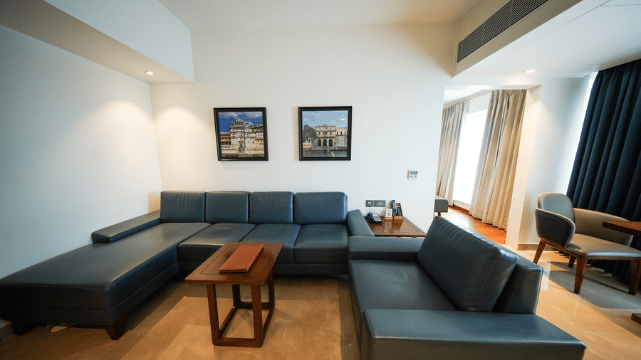 A view of the living area inside the Premium Suite Room at Pride Premier Udaipur. The space contains two sofas arranged around a low central table, with framed artwork hanging on the wall behind them.