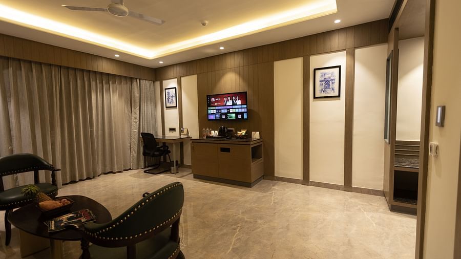 A cosy lounge area with chairs, a coffee table, and a TV mounted on the wall at Pride Resort, Jodhpur, under warm lighting.