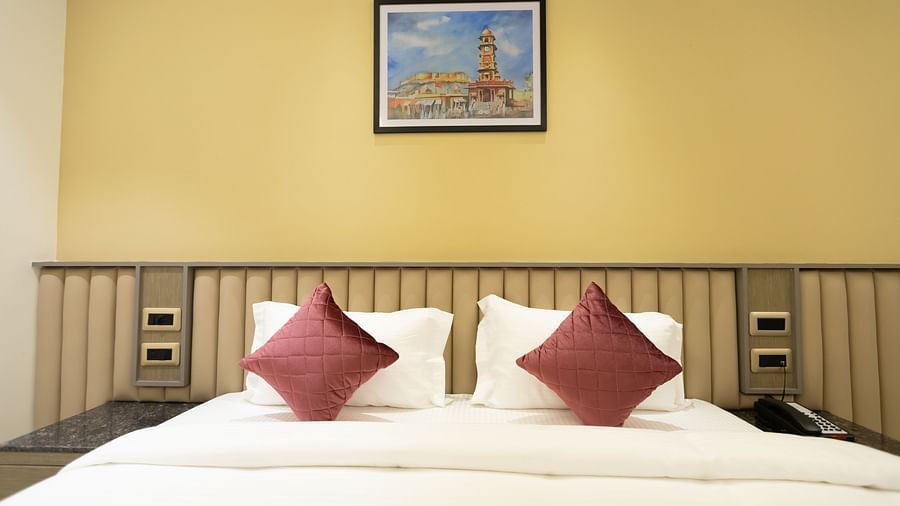 A neatly made bed with two cushions and a framed painting above the headboard at Pride Resort, Jodhpur.