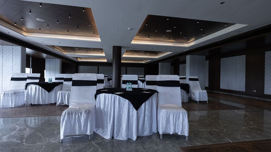 A spacious banquet hall at Pride Resort, Jodhpur, set up with tables and chairs covered in white and black cloth.