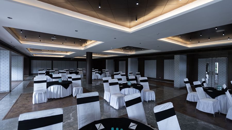 A large banquet hall at Pride Resort, Jodhpur, featuring multiple round tables and chairs with white covers and black accents.