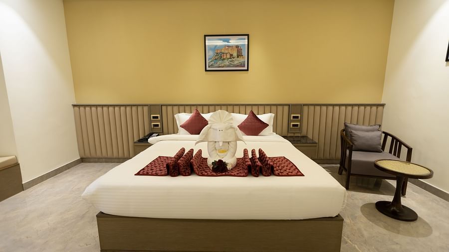 A neatly made bed with decorative towels and cushions in a spacious room at Pride Resort, Jodhpur, with framed artwork above.